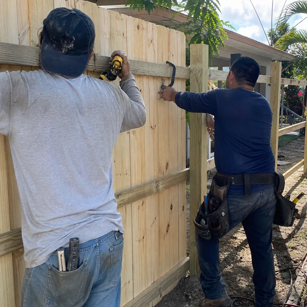 Two construction workers installing a wooden fence in a backyard